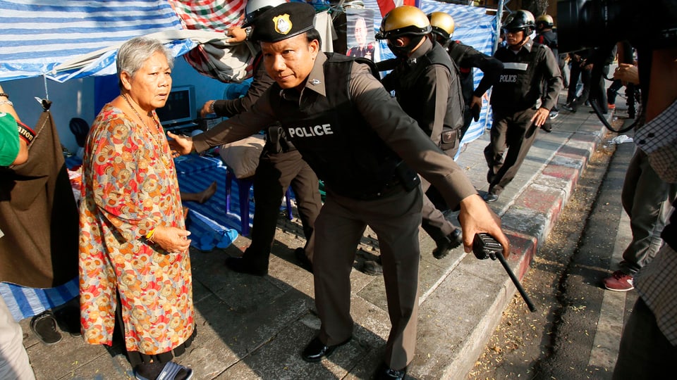 Ein thaliändischer Polizist bittet eine alte Frau zum Verlassen eines Protestcamps