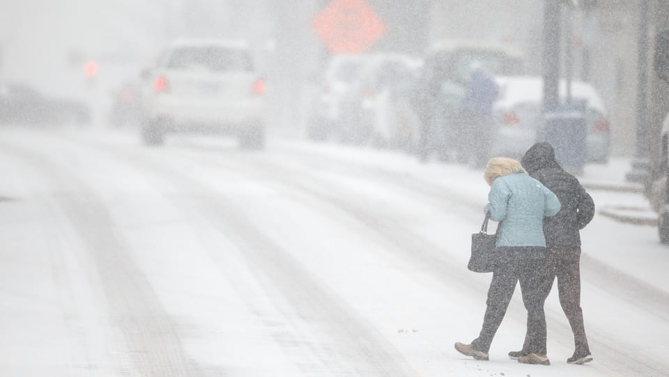 Zwei Menschen überqueren eine verschneite Strasse.
