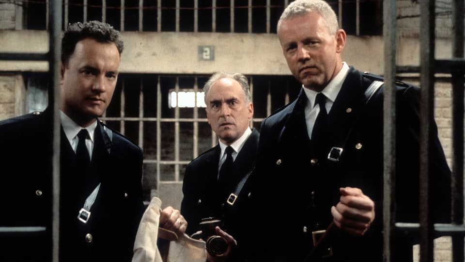 Drei Männer starren in eine Gefängniszelle.