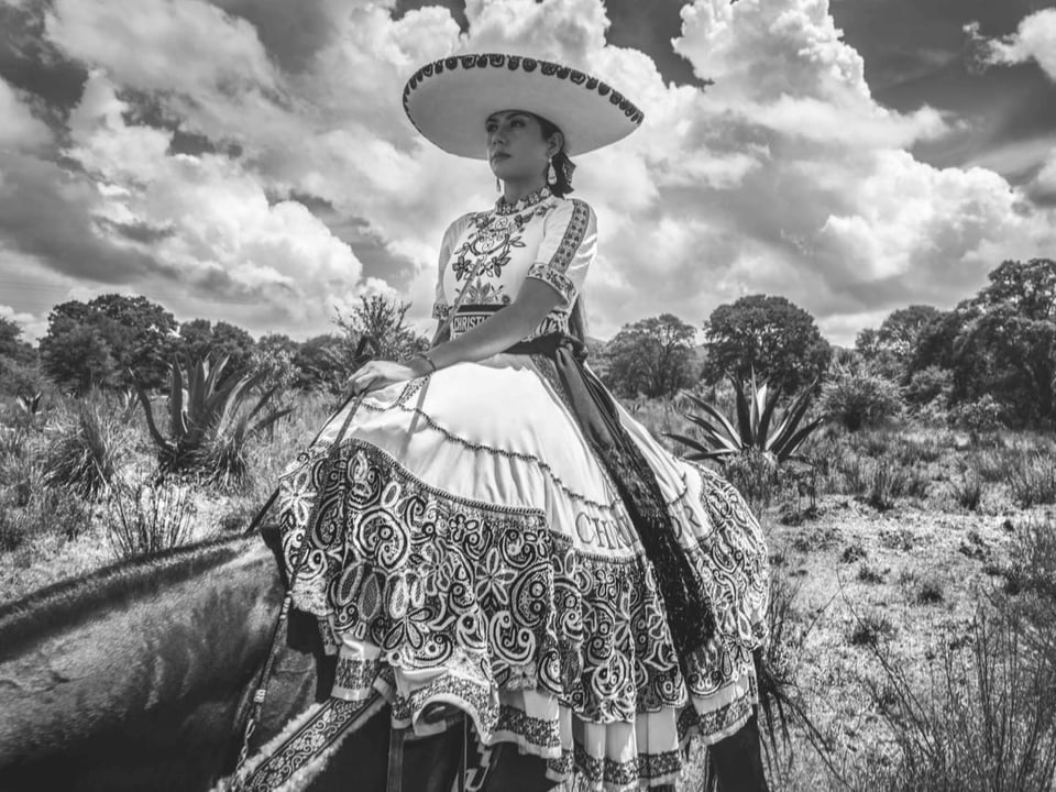 Frau reitet mit langem Kleid und Sombrero auf einem Pferd
