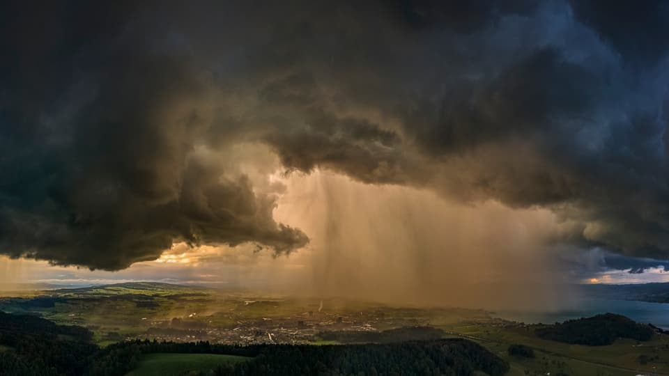 Dunkle Gewitterwolke mit starkem Regenschauer über Landschaft am See