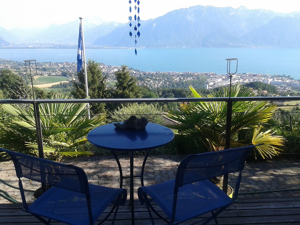 Balkon mit Tisch und zwei Stühlen, im Hintergrund der Genfersee.