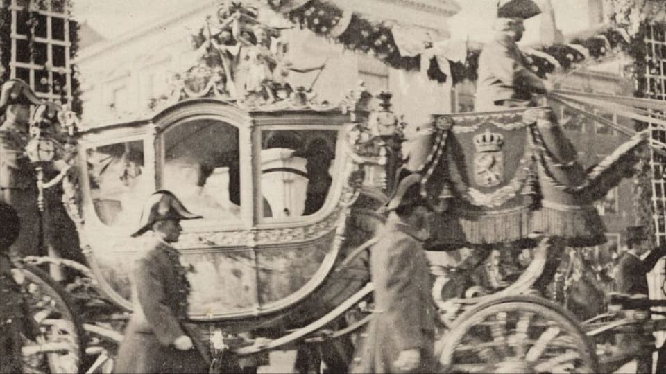 Eine alte Kutsche, begleitet von Männern in Uniform.