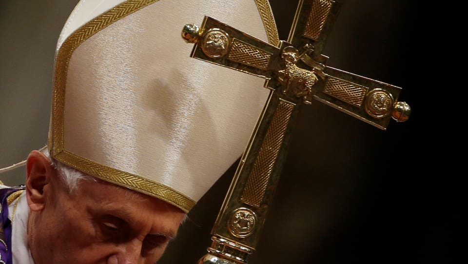 Papst mit einem Kreuz in der Hand, er steht gebückt.