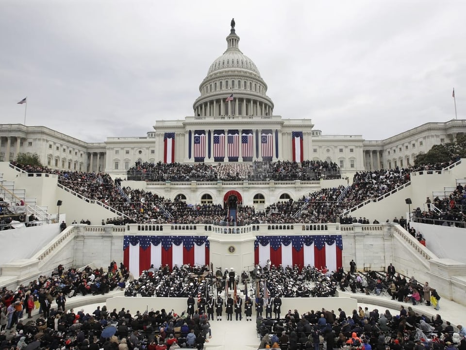 Ein Bild vom US-Kapitol. Es ist mit US-Flaggen geschmückt. Das Publikum verteilt sich vor dem Gebäude.