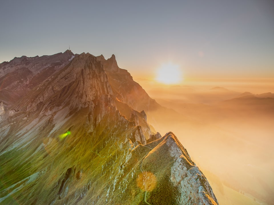 Gipfel bei Sonnenaufgang mit Dunst im Tal und wolkenlosen Verhältnissen darüber.