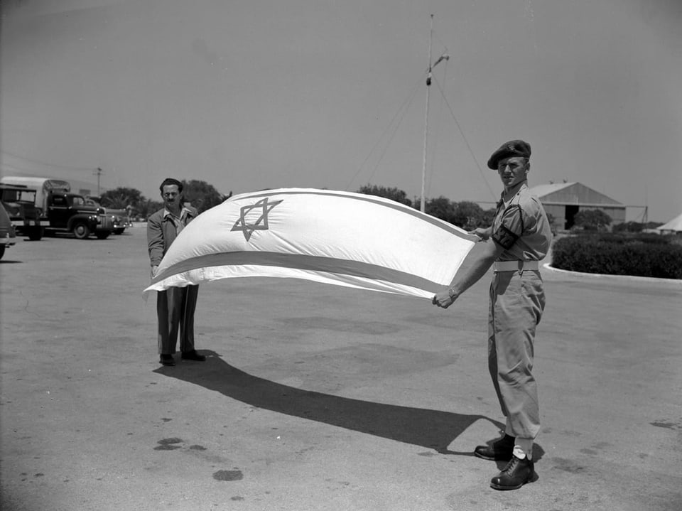 Zwei Männer halten die israelische Flagge auf einem Parkplatz. Foto in schwarz/weiss.