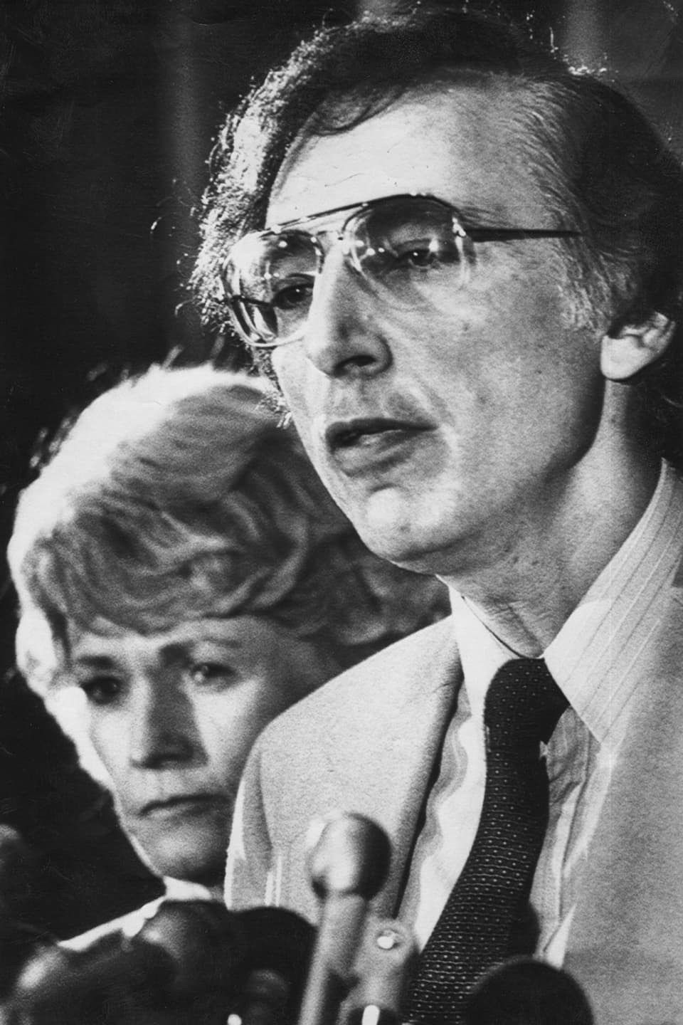 Ein Mann mit Brille und eine Frau stehen vor einem Mikrophon