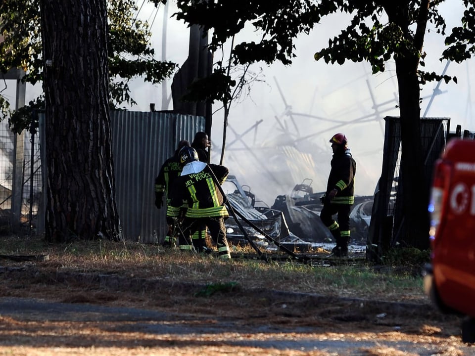 Feuerwehrleute versuchen Brand bei Autoschrottplatz unter Kontrolle zu bringen. Dichter Rauch ist zu sehen.