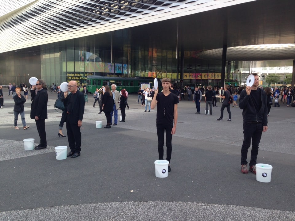 Eine Gruppe schwarz gekleideter junger Menschen steht im Kreis auf dem Platz und jede Person hölt einen Frisbee in der Hand