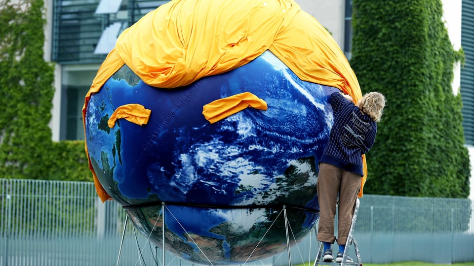 Eine Weltkugek ist mit einem gelben Tuch geschmückt, das die Frisur von Donald Trump darstellen soll.