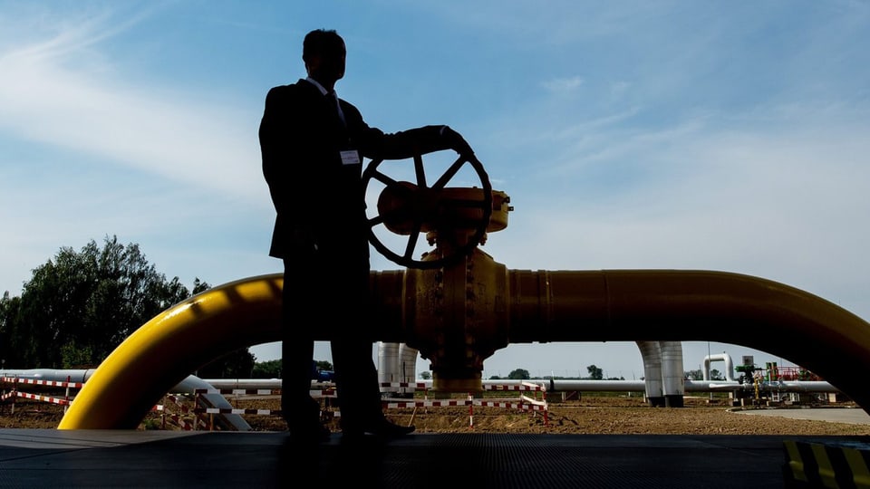 Mann im Gegenlicht dreht am Regulierungsrad einer Gaspipeline