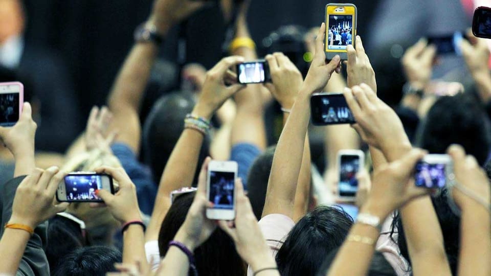 Viele Hände halten ein Smartphone in die Luft und filmen.