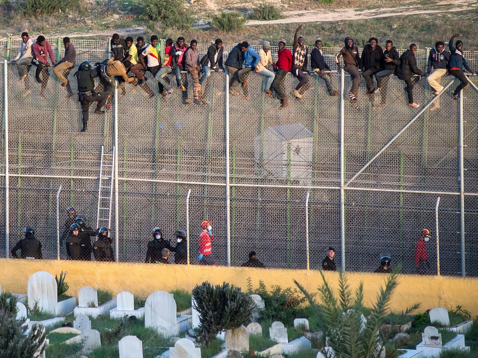 Flüchtlinge sitzen auf dem Grenzzaun im spanischen Melilla.