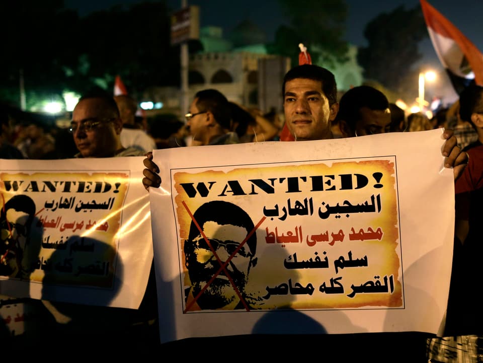 Ein Mann hält ein Plakat mit einem Foto Mursis, das durchgestrichen ist. 