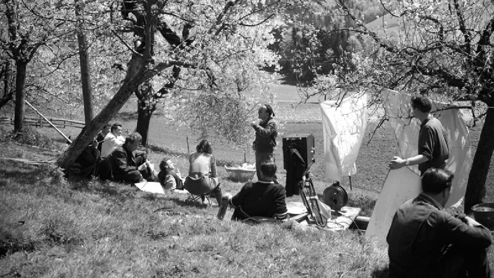 Die Crew bereitet sich auf eine Szene an der Wäscheleine vor. Alle sitzen im Gras, Franz Schnyder steht und hält eine Ansprache.