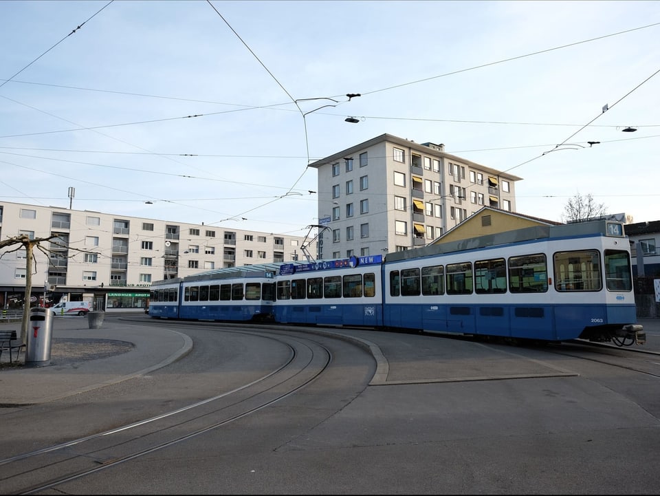 Blau-weisses Tram steht an der Endstation, im Hintergrund sind Wohnblöcke zu sehen.