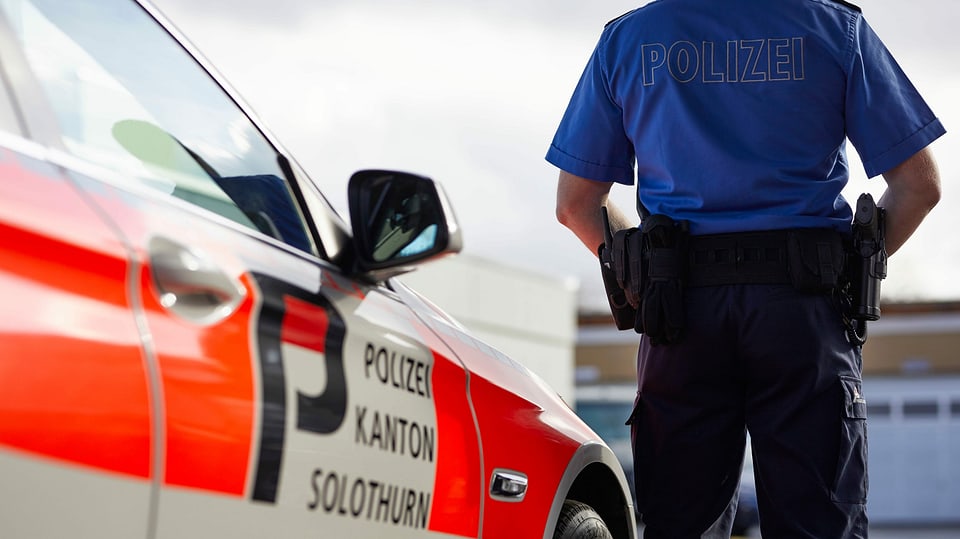Ein Polizist steht neben einem Polizeiauto mit der Aufschrift Polizei Kanton Solothurn.