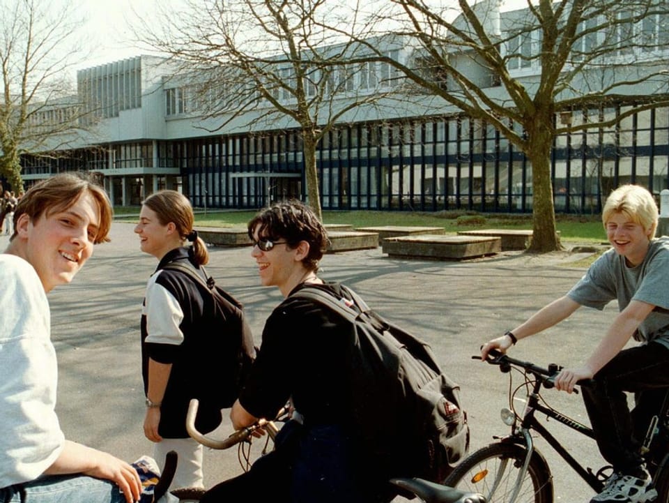 Fünf Schüler stehen lachend vor dem Gebäude der Kantonsschule Alpenquai. 