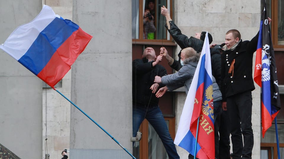 Demonstranten hissen eine russische Fahne bei einem Regierungsgebäude.