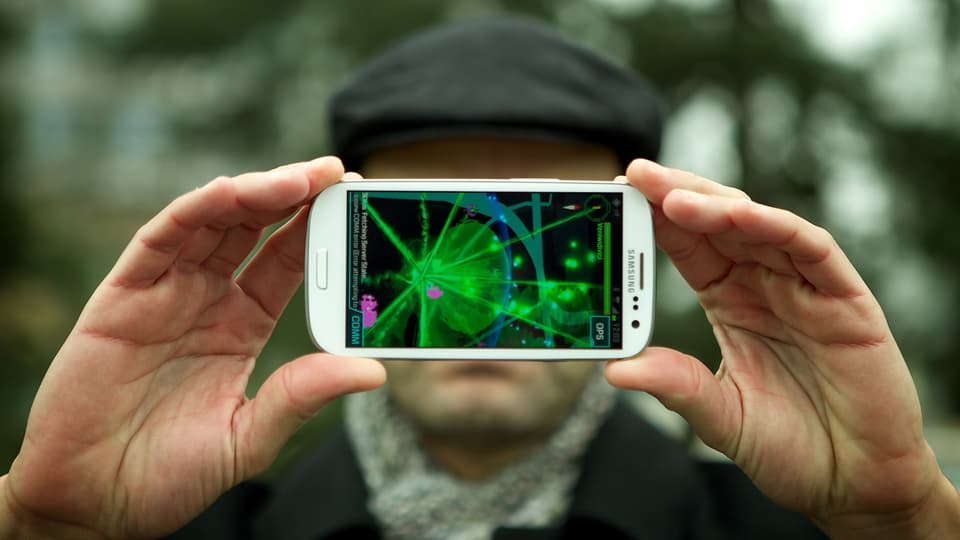 Reto Widmer von der SRF Digitalredaktion hält sein Smartphone in der Hand, auf dem ein Portal von Google Ingress beim Zürcher Bucheggplatz grün leuchtet.