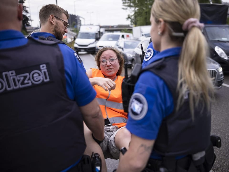 Polizisten tragen einen Klimaaktivistin mit Warnweste von der Strasse weg.