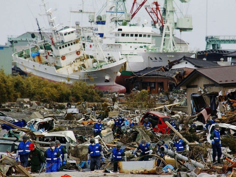 Schiffe auf dem Land und Trümmerhaufen, Menschen beim Aufräumen.