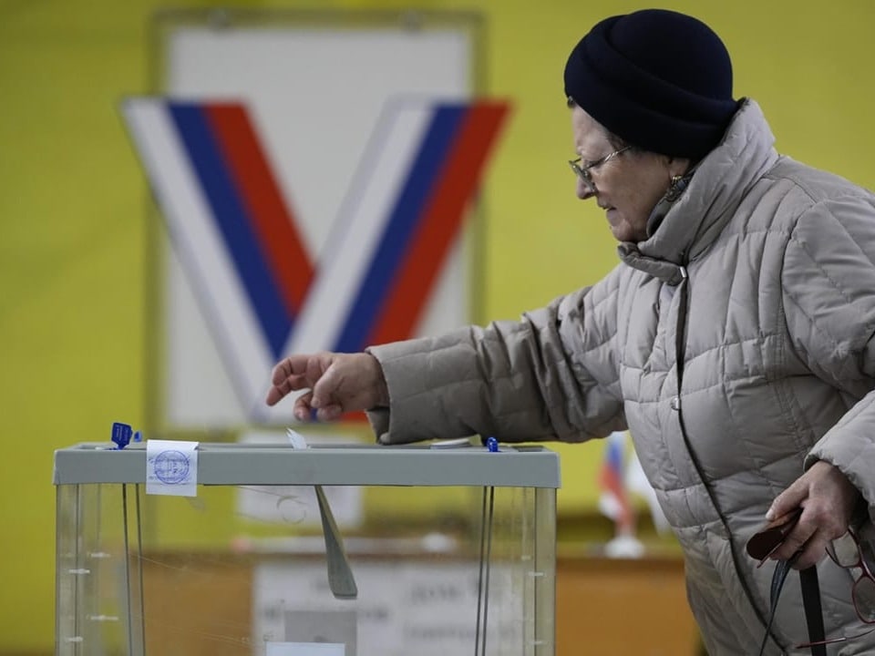 Eine Frau wirft in einem Wahllokal ihre Stimme in eine durchsichtige Urne