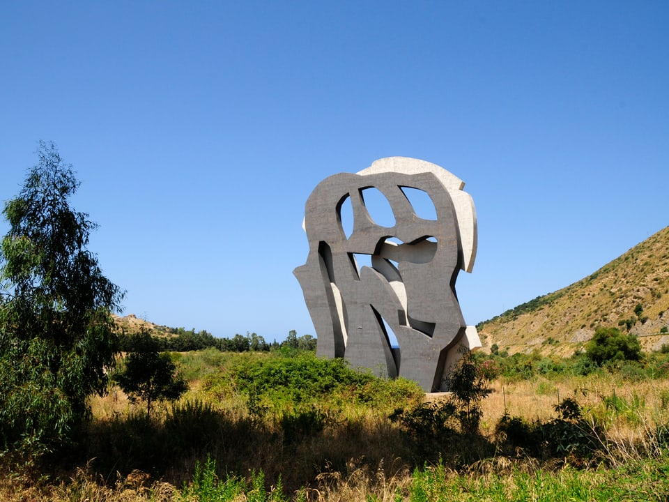 Eine Skulptur in einer Graslandschaft, bestehend aus zwei unterschiedlich gefärbten Stein-Formen.