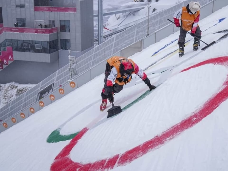 Helfer malen die olympischen Ringe in den Schnee.