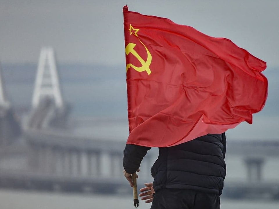 Meerenge zur Halbinsel Krim. Ein Mann steckt eine russische Flagge in einen Flaggenständer.