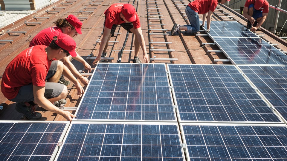 Ein paar Männer montieren Solarzellen auf einem Dach.