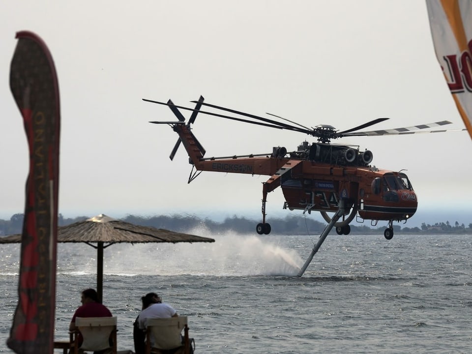 Ein Helikopter tankt nahe einem Strand Wasser auf.