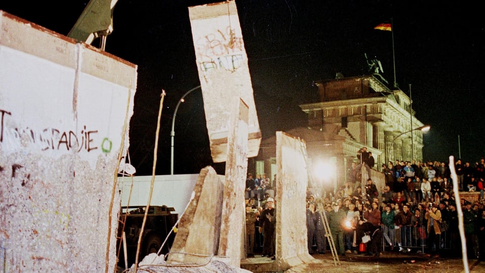 Der Abriss der Berliner Mauer beim Brandenburger Tor mit Baggern und vielen Zuschauern.