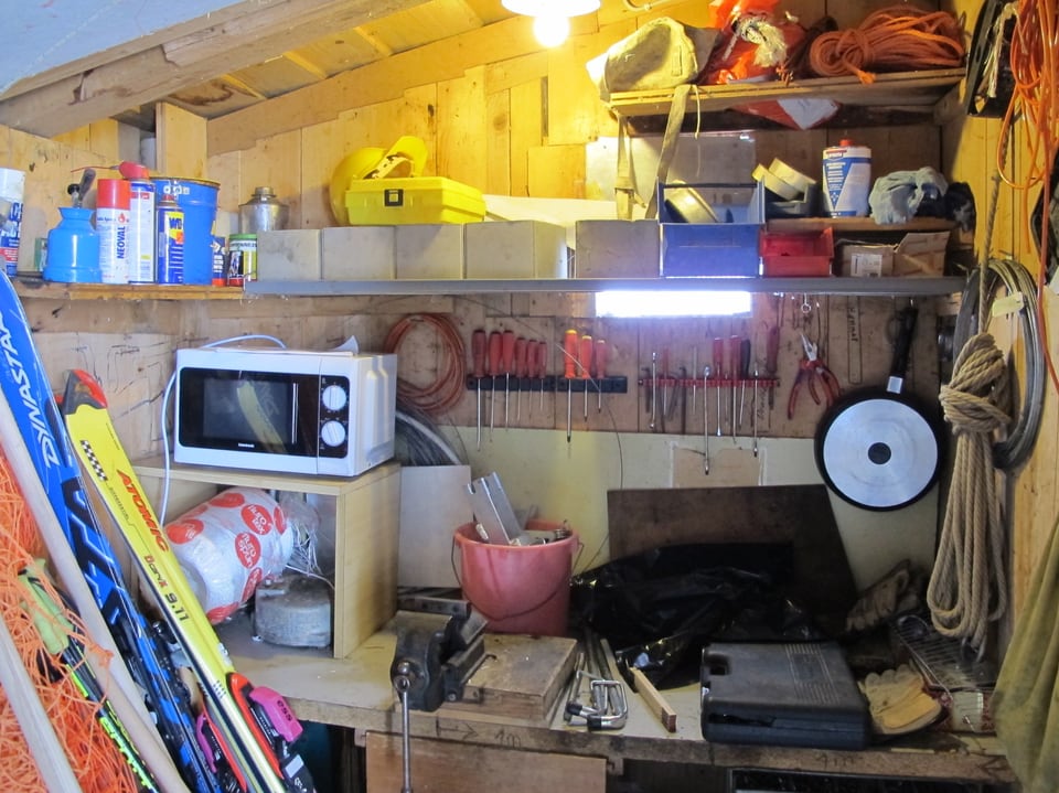 Blick in eine kleine Werkstatt mit diversen Werkzeugen, schummrigem Licht und einer Mikrowelle.