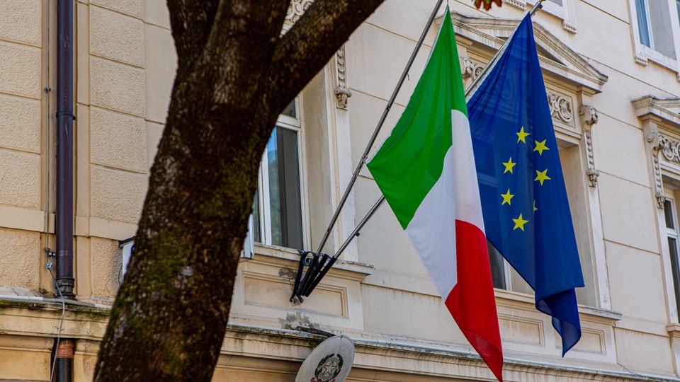 Die Flagge Italiens und der EU hängen an einer Hausfassade nebeneinander.