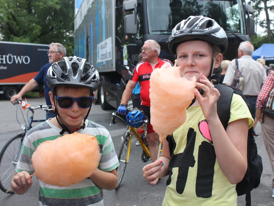 Kinder mit Velohelm und einer orangen Zuckerwatte in der Hand.