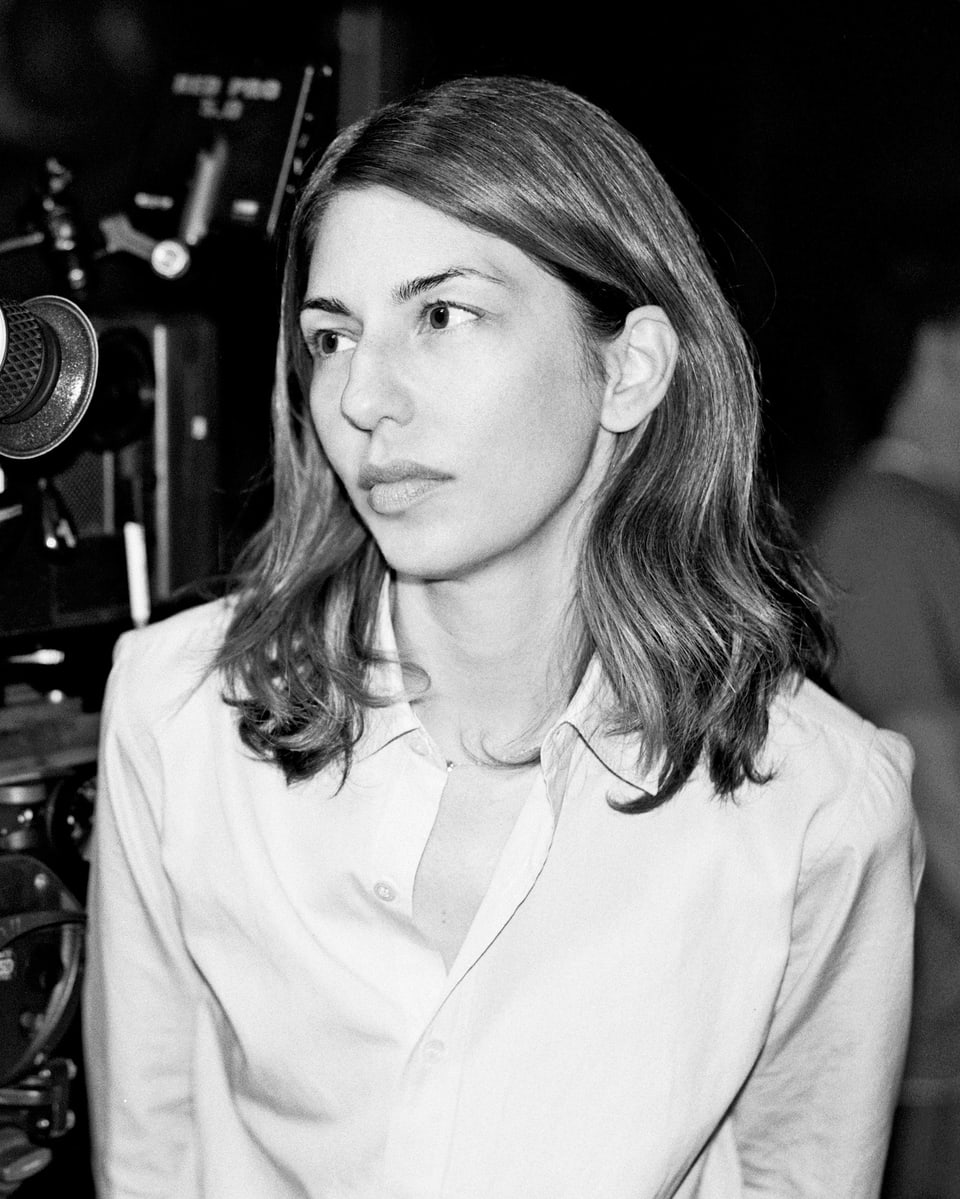 Die Regisseurin Sofia Coppola in weisser Bluse neben einer Kamera.