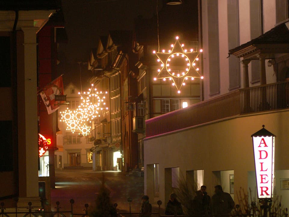 Blick in die Altstadt von Appenzell bei Nacht, leuchtende Weihnachtssterne hängen in der Gasse.