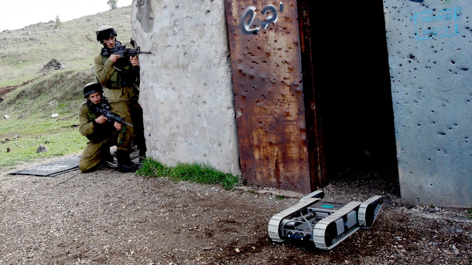 Ein Militärroboter sucht das Gelände ab, auf den Golanhöhen, im Hintergrund zwei israelische Soldaten.