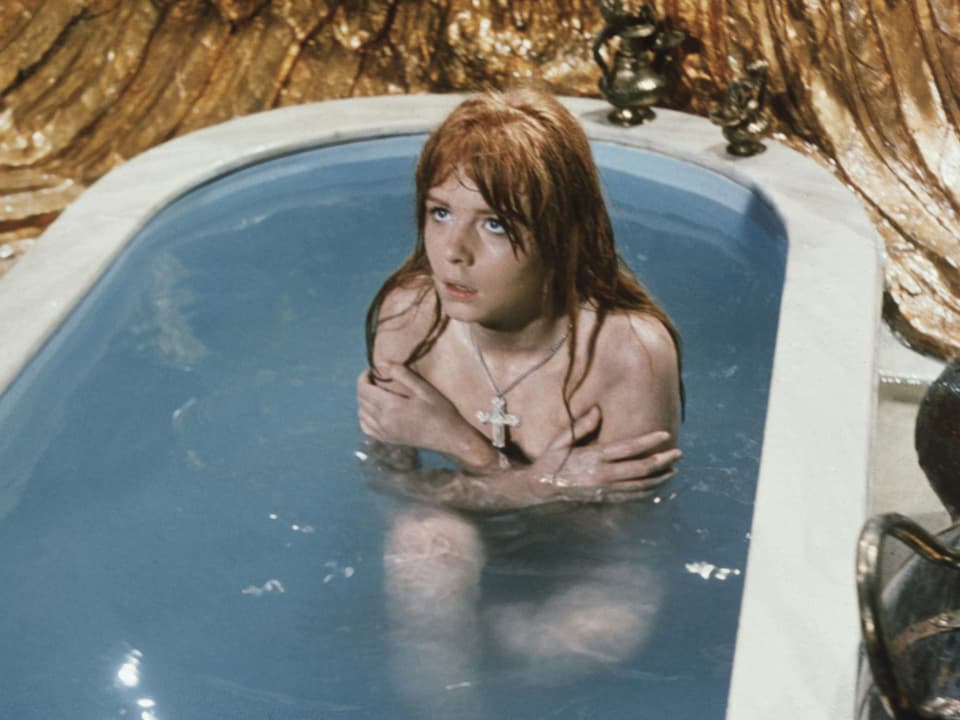 Eine junge Frau sitzt in einer Badewanne und bedeckt ihren Oberkörper.