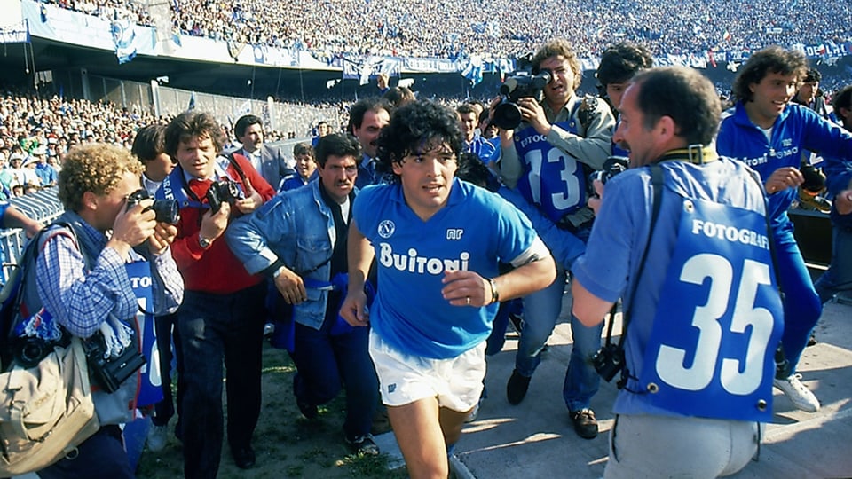 Der Fussballer Diego Maradona läuft umringt von Paparazzi vom Fussballplatz.