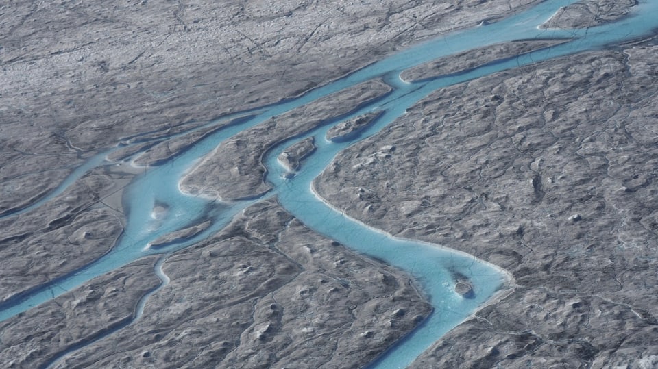 Luftaufnahme, grauer Gletscher, durchzogen von Schmelzwasser-Flüssen.
