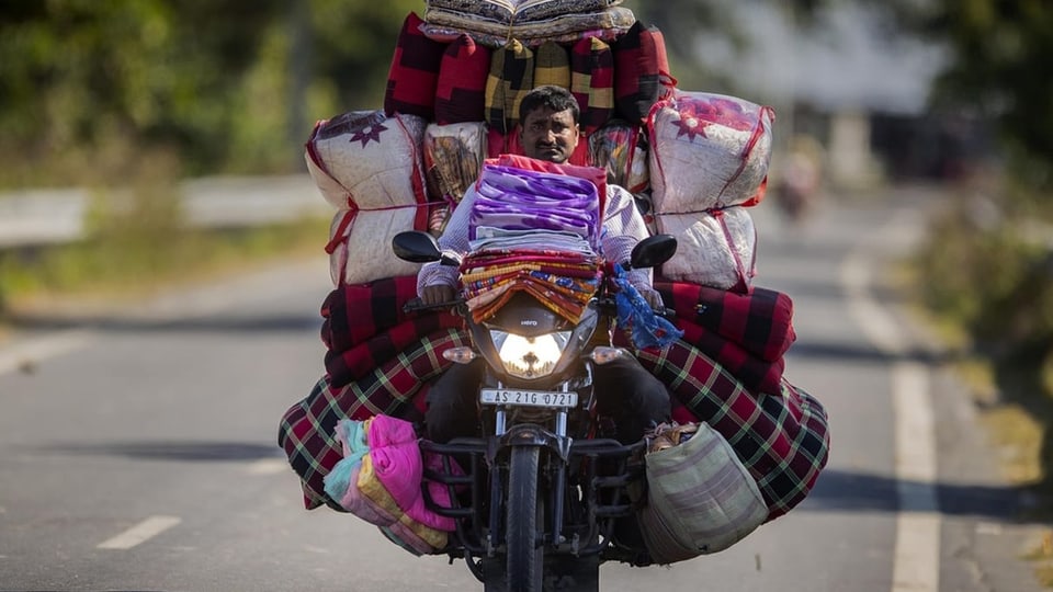 Ein Mann auf einem mit dicken Säcken beladenen Motorrad in Indien.