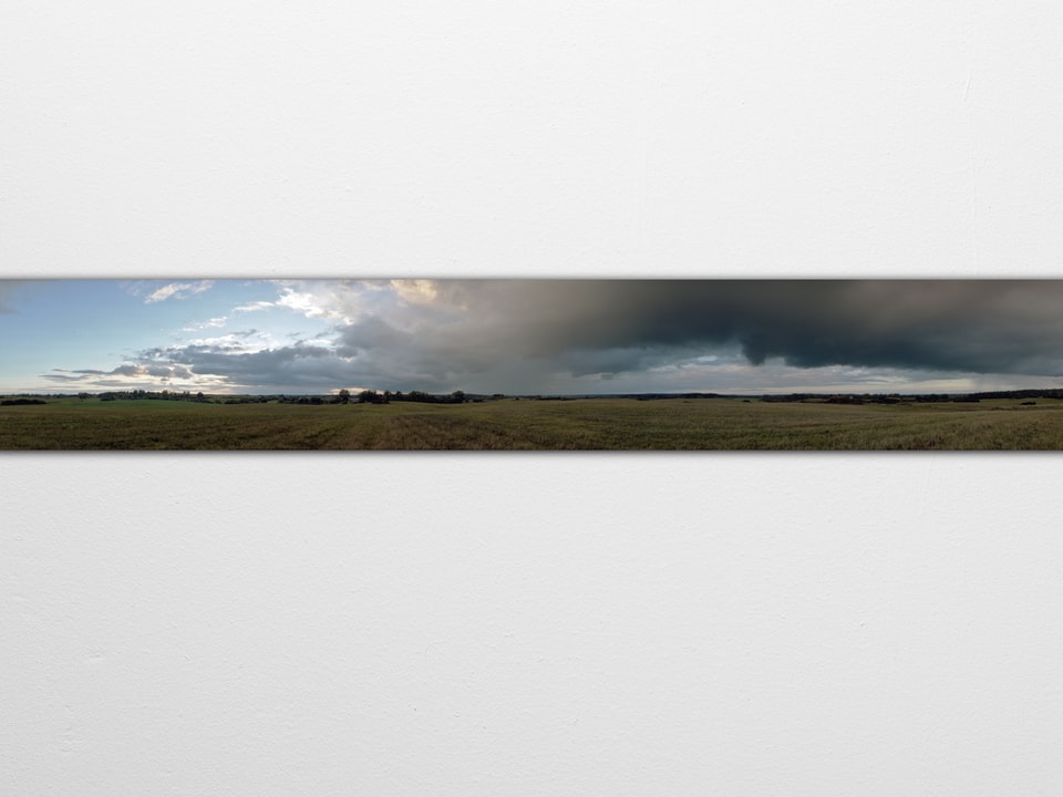 Panoramabild einer Landschaft: Links mit Sonnenschein, rechts Gewitterwolken.