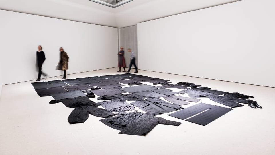 Ein Museumsraum: Auf dem Boden sind schwarze Kleider ausgebreitet.