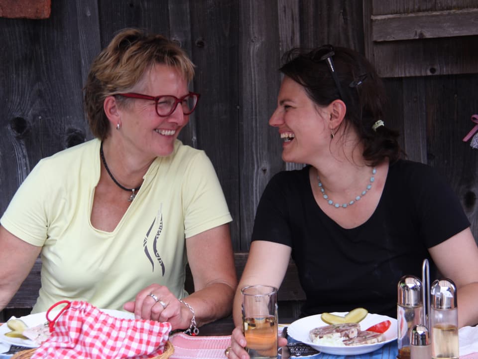 Die beiden Frauen sitzen am Tisch beim Mittagessen und führen ein fröhliches Gespräch.