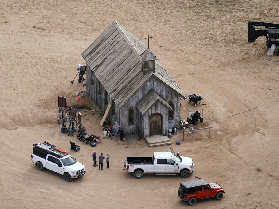 Luftaufnahme einer kleinen Kirche aus Holz in einer trockenen Landschaft. Um das Gebäude steht eine Filmcrew und Autos.