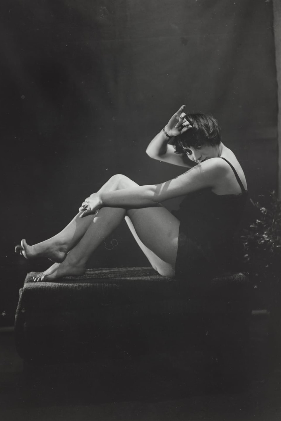 Frau mit kurzem Kleid, posiert sitzend, Arm über Kopf.