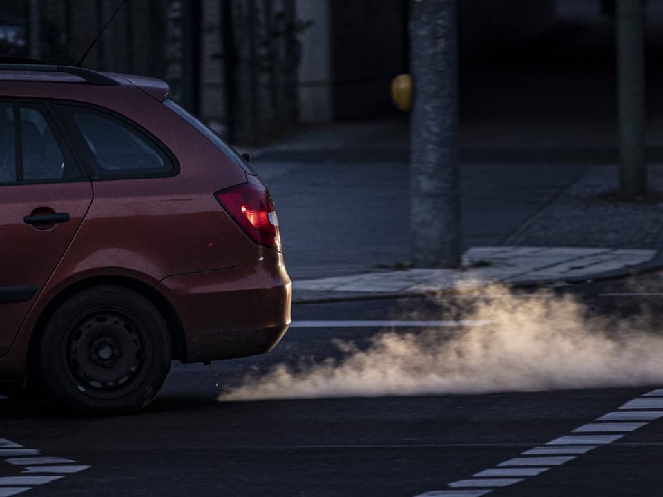 Rotes Auto fährt vorbei mit sichtbaren Abgasen.